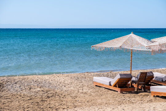 Wooden sunbeds and woven umbrellas on Komi sandy beach Chios island under bright sunshine