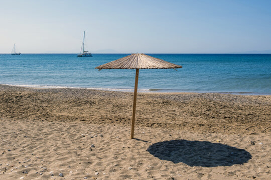Straw umbrella on the sand of Komi Beach, Chios Island, Greece. Summer sunny day and calm turquoise sea.