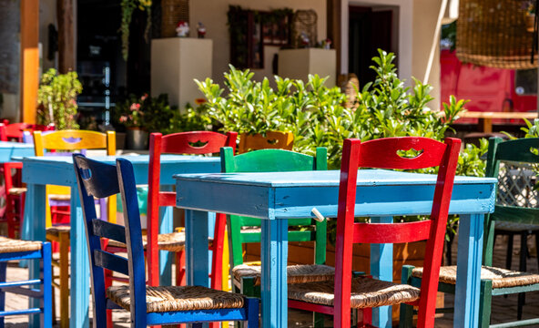 Colorful wooden chairs and tables in sunny Mediterranean outdoor cafe garden, summer day