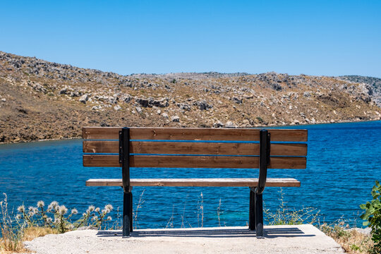Wooden bench overlooking blue coastal bay and rocky hills under blue summer sky
