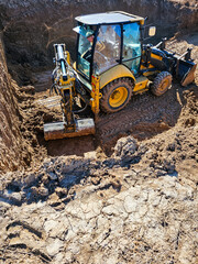 Fototapeta premium Compact backhoe loader digging soil inside deep construction excavation