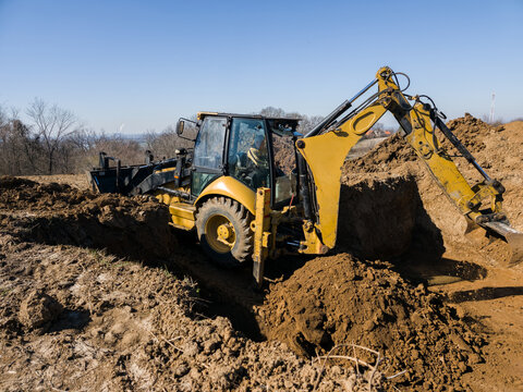 Backhoe loader performing excavation work for foundation in sunny landscape