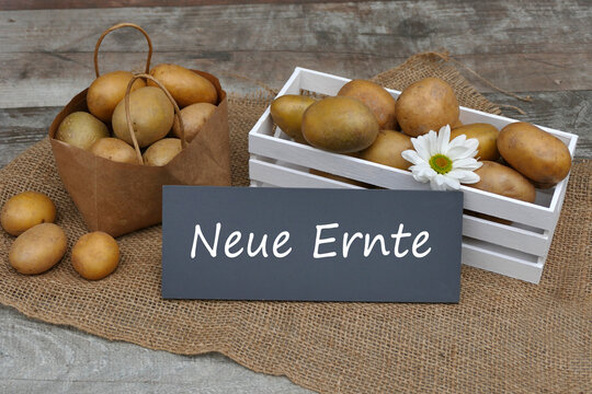 Frische Kartoffeln der neuen Ernte in Holzkiste und Papiert&uuml;te auf rustikalem Jutehintergrund.
