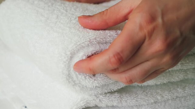 A close-up of a hand of maid arranging and smoothing white towels. The scene highlights hotel housekeeping, cleanliness, and professional service with fresh, neatly folded linens in a hospitality sett