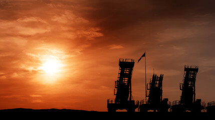 Obraz premium Missile defense system launchers standing against a vibrant sunset, a flag flying, conveying themes of geopolitical security and military strength