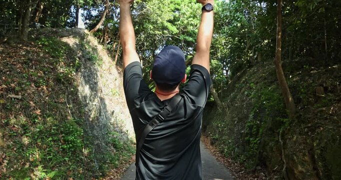 Back view of man with arms outstretched on lush forest trail. Wearing black activewear. Concept of freedom, achievement, and nature exploration.