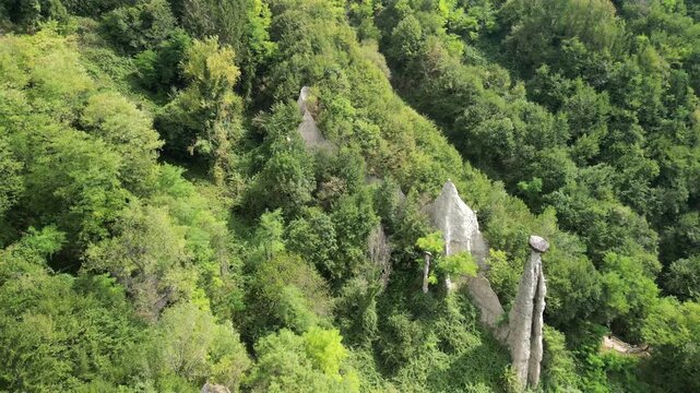Lake Iseo, drone reverse flight over Zone earth pyramids (Piramidi di Zone) in Italy, pulling back reveals hoodoo capstones and sandy cliffs in a deep green ravine