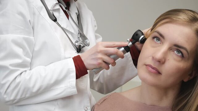 Doctor examining woman ear with otoscope during medical checkup in clinic patient consultation healthcare diagnostics indoors.