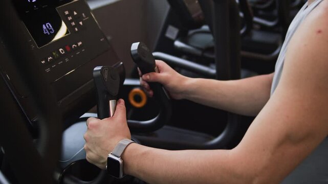Tilt shot of young Asian man using elliptical trainer while doing cardio after workout in modern gym