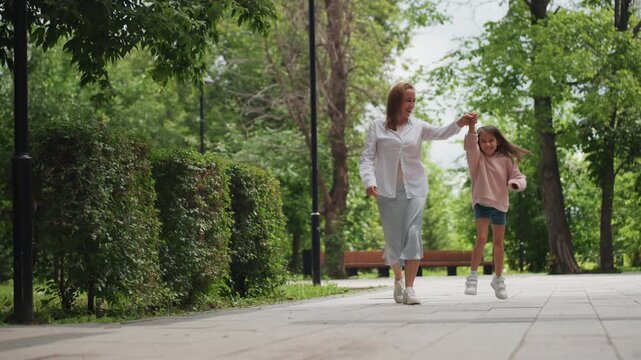 Casual stroll in park with smiling family members. Happy mother and child holding hands during sunny park outing. Unposed snapshot capturing mother and daughter sharing cheerful moment in park