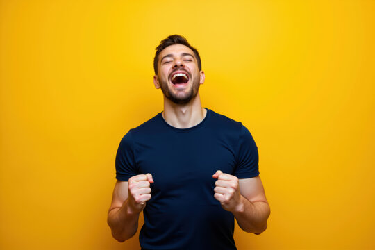 A man wearing a dark blue shirt is laughing heartily with his eyes closed and fists clenched in front of a bright yellow background.