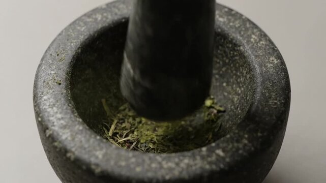 Close-up of dried herbs being crushed in a stone mortar and pestle for cooking or medicine.