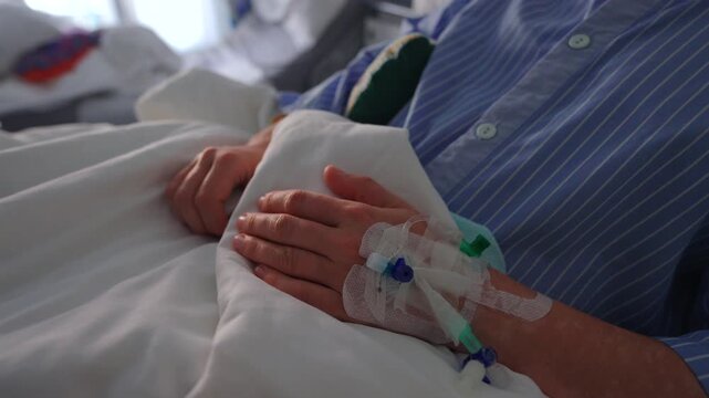 Close up of female patient hand with intravenous catheter secured by medical tape, resting on hospital bed, conveying treatment process, fragility and clinical care