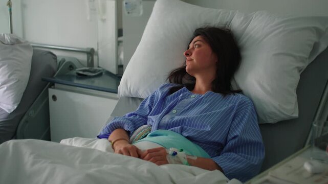 Female patient resting in hospital bed after surgery looking to side with calm expression and intravenous line showing recovery and quiet awareness in medical room