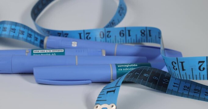 Sliding view of semaglutide glp-1 injection pens with a blue tape measure on white for representing medical weight loss and diabetes.