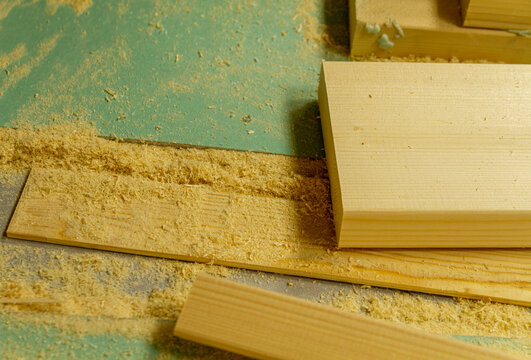 The image shows a woodworking workshop scene with raw lumber pieces scattered on a workbench covered in sawdust, showcasing the process of constructing a mortise and tenon joint. Craft
