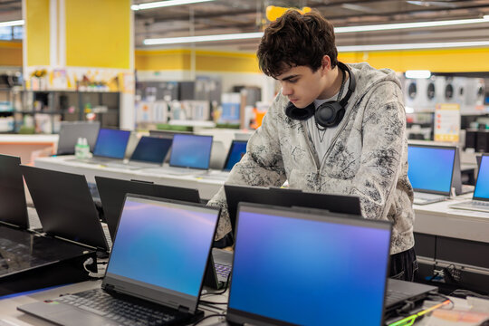 Teenage boy comparing laptops in an electronics store and choosing a device. Technology shopping, education, digital lifestyle and consumer purchase decision concept