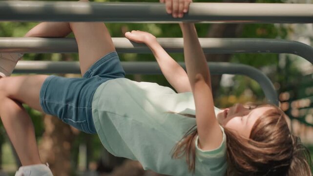 Daughter climbing metal bars at playground in sunlit park, inverted pose with loose braids and focused grip, energetic movement and joyful expression, candid adventurous play showcasing balance