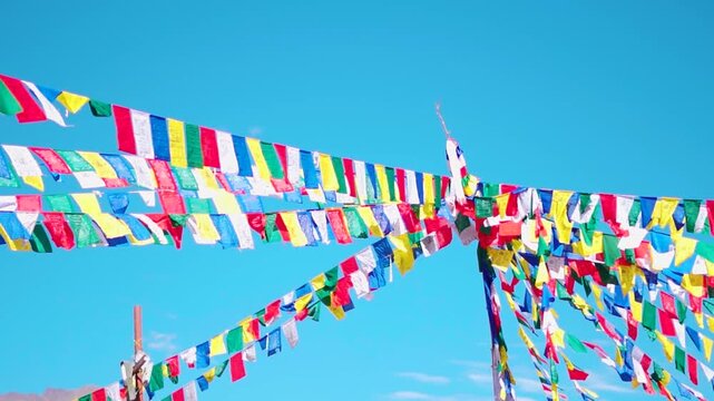 Handheld shot of colorful Buddhist prayer flags against the clear blue sky as seen from Padum town in Zanskar Valley of remote Ladakh, India. Buddhist prayer flags waving in the wind during autumn.