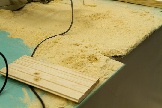 The image shows a woodworking workshop scene with raw lumber pieces scattered on a workbench covered in sawdust, showcasing the process of constructing a mortise and tenon joint. Craft