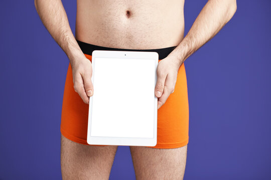 Urology. Man in orange underwear with tablet on purple background, closeup
