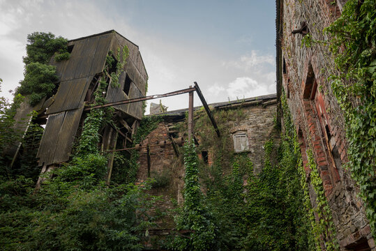 Ruins of an abandoned, industrial building shows crumbling stone and brick, with boarded-up windows. Photo taken in Inniskeen, County Monaghan, Ireland