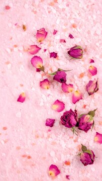 Dried rose buds and petals scattered on a bed of pink bath salts
