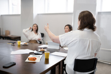 Obraz premium Woman giving presentation and gesturing as others listen during business breakfast at office table. Presentation, gesturing, business, breakfast, office, teamwork.