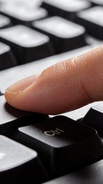Vertical video: Hovering fingertip lowering onto Ctrl key at desk, depressing black keycap gently