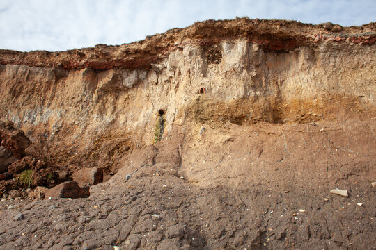 Crumbling boulder clay cliffs on the East Yorkshire Coast UK, one of the fastest eroding coastlines in Europe showing exposed and falling plumbing pipework