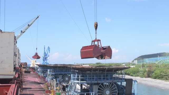 crane with a clamshell grab lifts bulk material at a port, showing cargo handling on a ship deck with industrial equipment and conveyors in the background