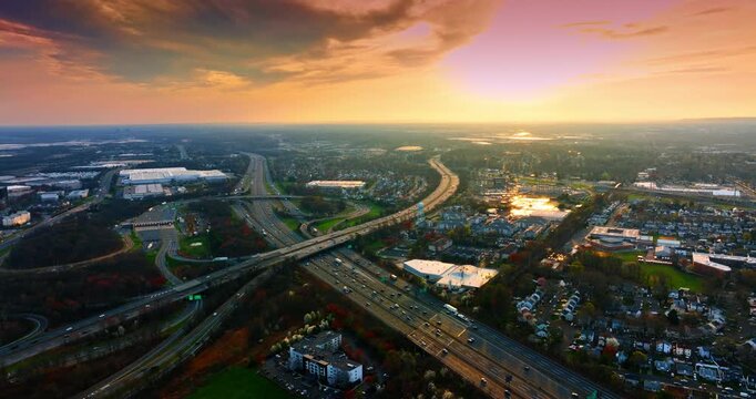 Sunset cloudy sky over the vast scenery of the city. Multiple cars go by the motorways and trestles. Aerial view.