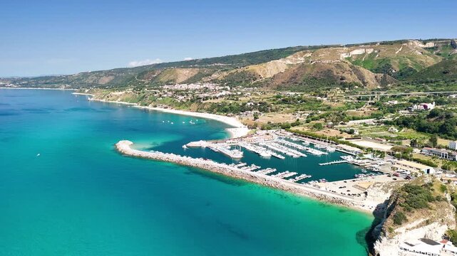 Breathtaking aerial view of Tropea's charming port, showcasing colorful fishing boats and elegant yachts moored in the calm turquoise waters of the Tyrrhenian Sea