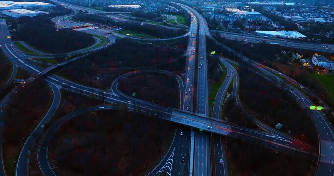 Huge modern interchange in the wooded area. Footage over the intersection at dusk time.