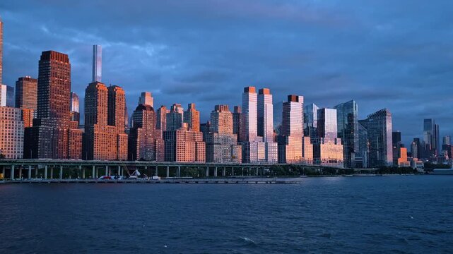 Light of setting sun on the facades of glass skyscrapers. View on the towers of Manhattan from the river at sunset.