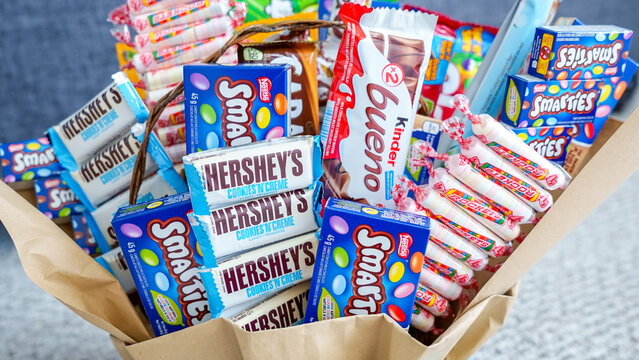 Colorful chocolate gift basket filled with assorted candies including Hershey's, Kinder Bueno, and Smarties on a textured background