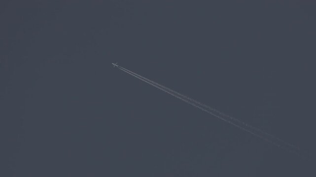 The journey begins, plane flies high in the blue sky, leaving a white trail. Jet airplane flying overhead in clear blue sky and leaving contrail. Slow motion 120 fps ProRes 422 10 bit C-LOG2 video.