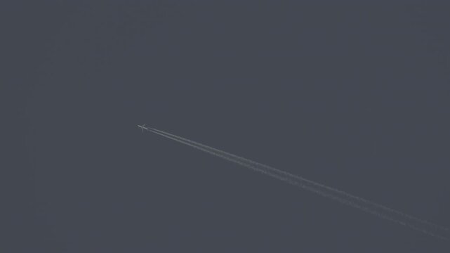 The journey begins, plane flies high in the blue sky, leaving a white trail. Jet airplane flying overhead in clear blue sky and leaving contrail. Slow motion 120 fps ProRes 422 10 bit C-LOG2 video.