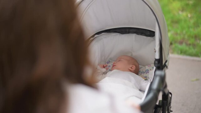 White mother watching baby in stroller, hands on handle and attentive gaze, canopy shadow and park greenery in background, protective nurturing mood, intimate lifestyle moment emphasizing bond