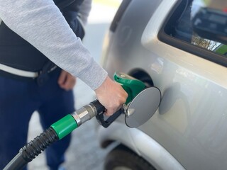 A detailed close-up shot capturing a person’s hand holding a green fuel pump nozzle and inserting it into the fuel tank of a silver car © Naty