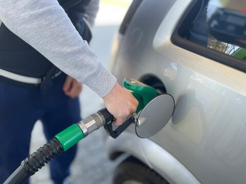 A detailed close-up shot capturing a person&rsquo;s hand holding a green fuel pump nozzle and inserting it into the fuel tank of a silver car