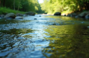 Fototapeta premium Flowing river water reflects green trees and blue sky. Sunlight plays on gentle waves. Smooth stones line the riverbed. Nature scene offers calm and tranquility.