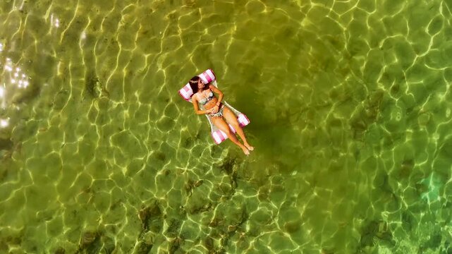 Drone perspective of a woman relaxing on inflatable mattress in stunning ocean waters