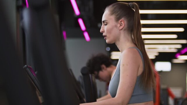 Tilt shot of young Caucasian woman using brand new elliptical trainer, doing cardio on it in gym cardio zone