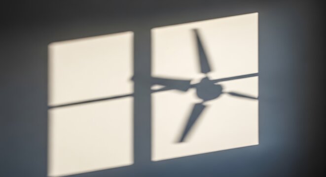 shadow of ceiling fan with four blades projected onto two lit rectangular window panes creating interesting visual effect indoor scene abstract representation