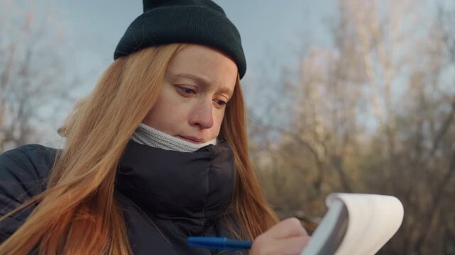 White woman pen poised outdoors, redhead witness reflects on snatcher encounter, closeup portrait reveals tearful gaze and pensive expression, scarf and coat visible, cold winter light, diary notation