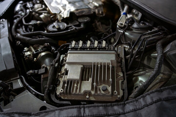 Fototapeta premium Automotive engine compartment with electronic control unit, wiring harnesses, and mechanical parts under an open hood, photographed in low light.