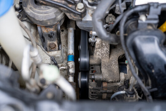 Close view of car engine belt drive with alternator, pulleys, and rotating components during operation in an automotive engine compartment.