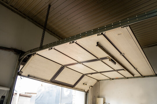 Interior view of an open sectional garage door with metal tracks and ceiling panels, showing workshop entrance and overhead mechanism.