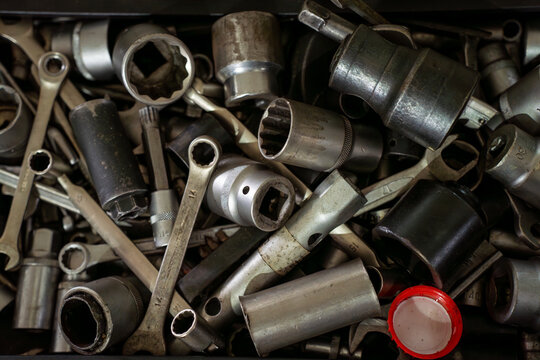 Close view of mixed socket heads and wrenches in a tool drawer, showing used metal hand tools for automotive repair and mechanical maintenance.